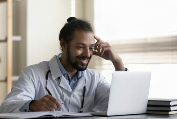 A male healthcare worker reviews an October job report on his computer