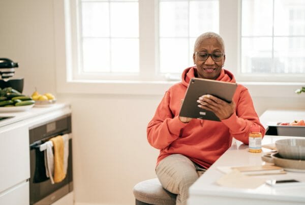Healthcare trends. A woman smiles at something on her tablet while sitting in a kitchen.